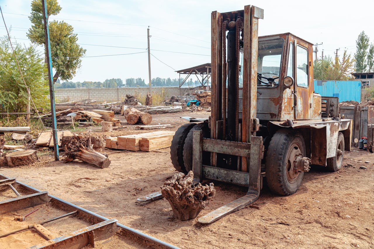 Old forklift in a rustic sawmill setting, surrounded by logs and lumber, hinting at heavy industry.